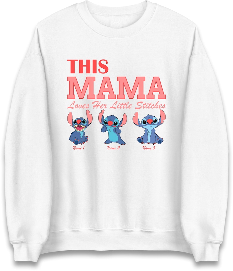 May include: White sweatshirt with the text "THIS MAMA" in red and pink lettering. Below the text are three blue cartoon characters with the text "Name 1", "Name 2", and "Name 3" below each character. The text "Loves Her Little Stitches" is below the word "MAMA".