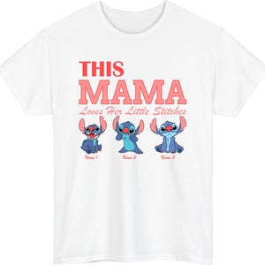 May include: White t-shirt featuring the text "THIS MAMA Loves Her Little Stitches" in red and pink. Below the text are three blue cartoon characters. The shirt is a crew neck style.
