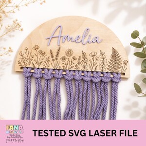 May include: A wooden wall hanging with the name "Amelia" in lavender script. The wooden semi-circle has a floral design and is connected to lavender macrame. The text "TESTED SVG LASER FILE" is at the bottom.