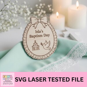 May include: A wooden baptism day sign with the text "Isla's Baptism Day" and a bow at the top. The sign features a church and a dove carrying an olive branch. The sign is on a mint green cloth with white lace trim.