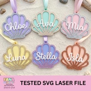 Puede incluir: Seis adornos en forma de concha en colores pastel, cada uno con un nombre diferente en escritura blanca. Las conchas tienen detalles de purpurina y están suspendidas por cintas. El texto "TESTED SVG LASER FILE" está en la parte inferior.