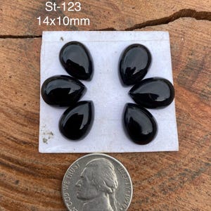 Könnte beinhalten: Sechs polierte, schwarze, tropfenförmige Edelsteine, angeordnet auf einer weißen Oberfläche. Die Edelsteine sind ca. 1,4 cm x 1,0 cm groß. Eine US-Nickel-Münze befindet sich im Vordergrund. Der Text "St-123" und "14x10mm" ist sichtbar.