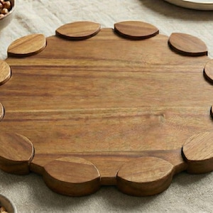 May include: A wooden serving board with a unique scalloped edge design. The board is surrounded by small bowls filled with olives and nuts. A glass of beer sits nearby, suggesting a casual gathering.