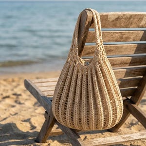 Pode incluir: Uma bolsa de crochê bege com um padrão de nervuras verticais e design aberto. A bolsa possui duas alças integradas e um fecho de botão de pressão metálico no centro superior, confeccionada com um material de fio de cor clara.