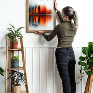 May include: A framed art print with a landscape design featuring a forest and its reflection in a lake. The artwork has a colour palette of orange, red, and grey. The words "smart" and "Life" are printed on the artwork. The frame is made of wood.