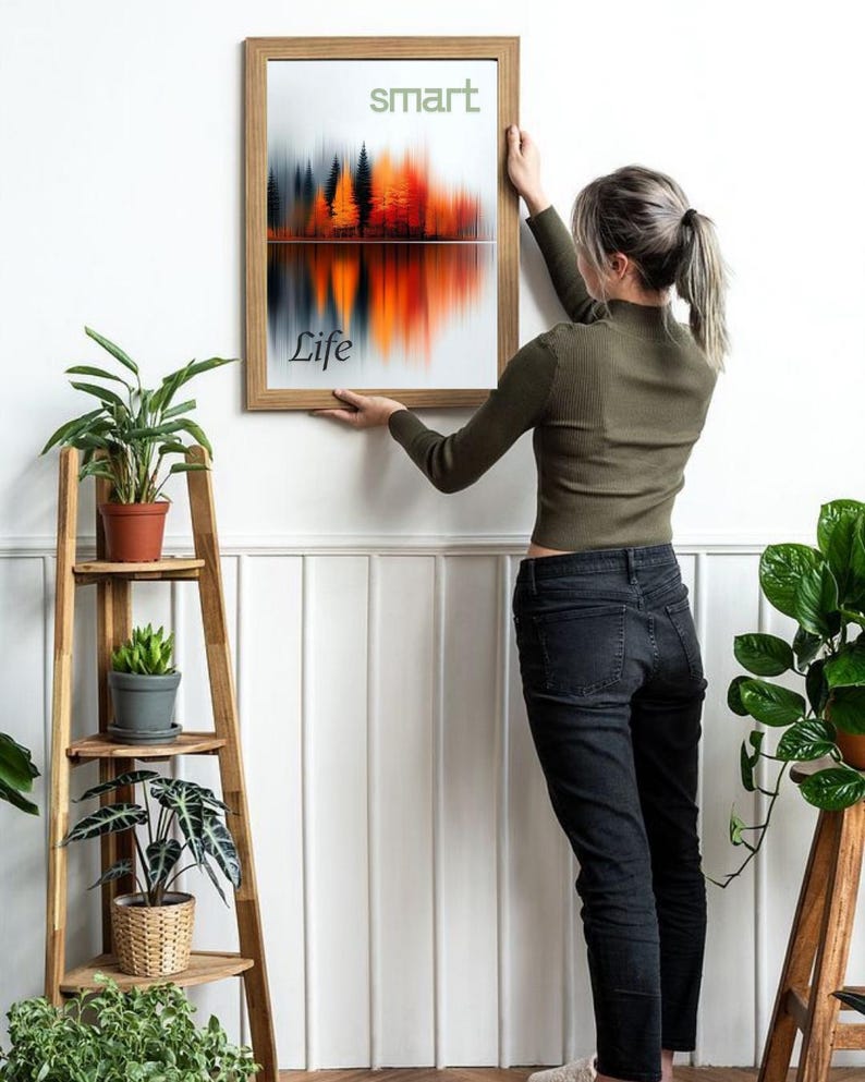 May include: A framed art print with a landscape design featuring a forest and its reflection in a lake. The artwork has a colour palette of orange, red, and grey. The words "smart" and "Life" are printed on the artwork. The frame is made of wood.