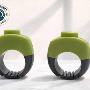 May include: Two green and black pet grooming tools. The tools have a ring-like design with a textured edge and a small, rounded top. The Cozy Paws Pet Apparel logo is in the upper left corner.