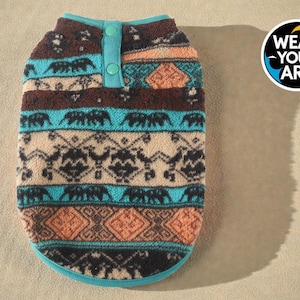 May include: A patterned dog sweater with a teal collar and button closure. The sweater features a repeating elephant design in teal, brown, and beige. The Wear Your Art logo is visible in the upper right corner.