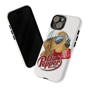 May include: White phone case featuring a cartoon dog wearing sunglasses and a backwards cap, holding a Dr. Pepper can. The Dr. Pepper logo is prominently displayed below the dog. A black phone is visible in the background.