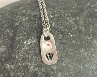 May include: A silver chain necklace with a small silver charm. The charm is shaped like a rectangle and has the letter "W" engraved on it. The charm also has a small clear stone in the center.
