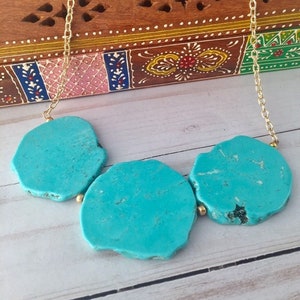 May include: A turquoise stone necklace with three large, irregularly shaped stones connected by a gold chain. The stones have a mottled, natural appearance.