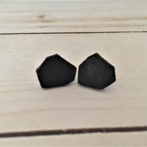 May include: A pair of black geometric stud earrings. The earrings are shaped like a pentagon with rounded edges.