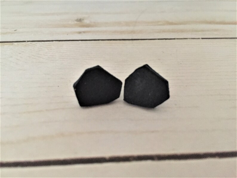 May include: A pair of black geometric stud earrings. The earrings are shaped like a pentagon with rounded edges.