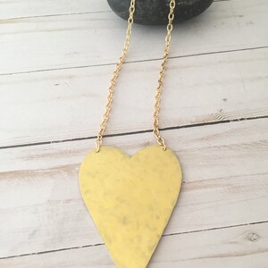Op de afbeelding: Een gouden ketting met een grote, gehammerde messing hart hanger.