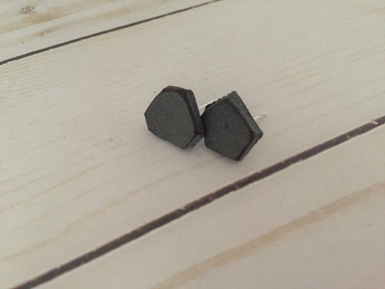 May include: A pair of gray leather stud earrings with a hexagonal shape.