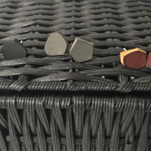 May include: Assortment of geometric shaped earrings in black, gray, and brown leather. The earrings are displayed on a black wicker surface.