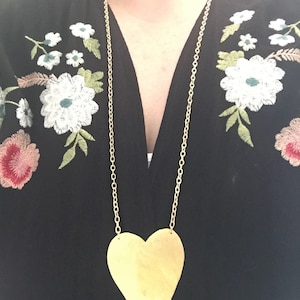 Op de afbeelding: Een gouden ketting met een grote, platte, gouden hart hanger.