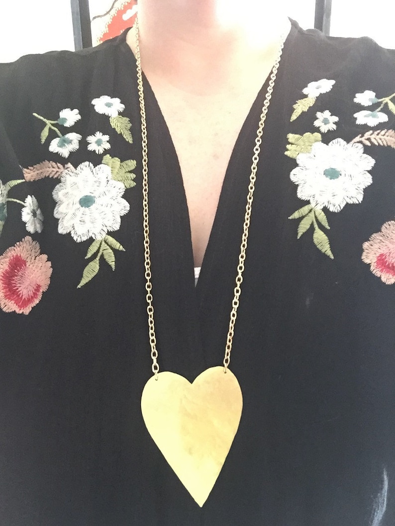 Op de afbeelding: Een gouden ketting met een grote, platte, gouden hart hanger.