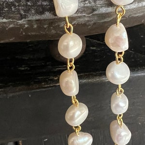 Pu&ograve; includere: Un paio di orecchini pendenti dorati con perle bianche. Gli orecchini sono realizzati con una catena delicata con pi&ugrave; perle bianche che pendono.