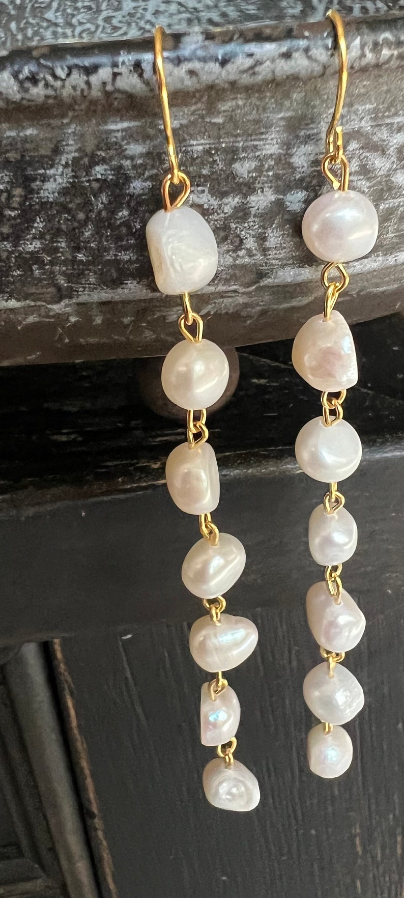 Pu&ograve; includere: Un paio di orecchini pendenti dorati con perle bianche. Gli orecchini sono realizzati con una catena delicata con pi&ugrave; perle bianche che pendono.