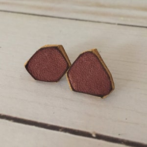 May include: A pair of small, hexagonal shaped earrings made of leather. The earrings are a deep burgundy color with a light brown border.