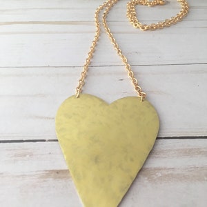 Op de afbeelding: Een gouden ketting met een hartvormige hanger met een gehammerde textuur. De ketting is ook goud.