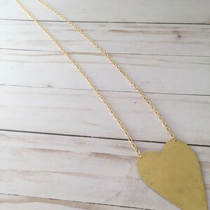 Op de afbeelding: Een gouden ketting met een grote, platte, gouden hart hanger.