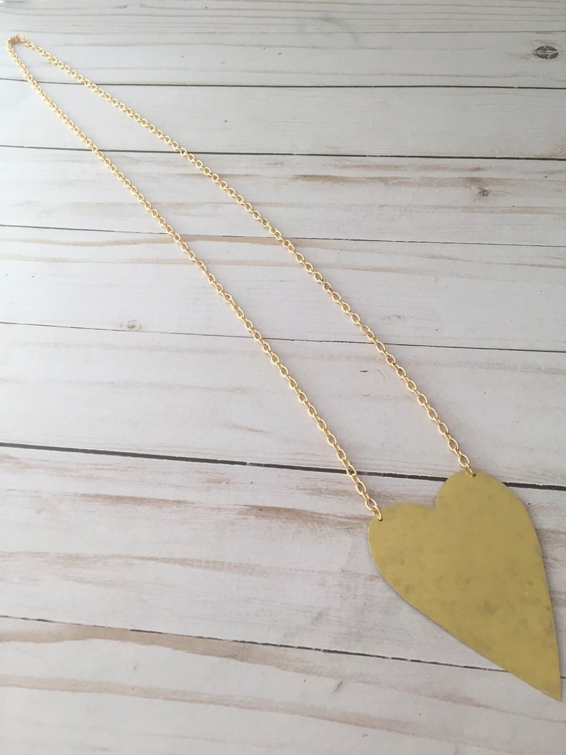 Op de afbeelding: Een gouden ketting met een grote, platte, gouden hart hanger.