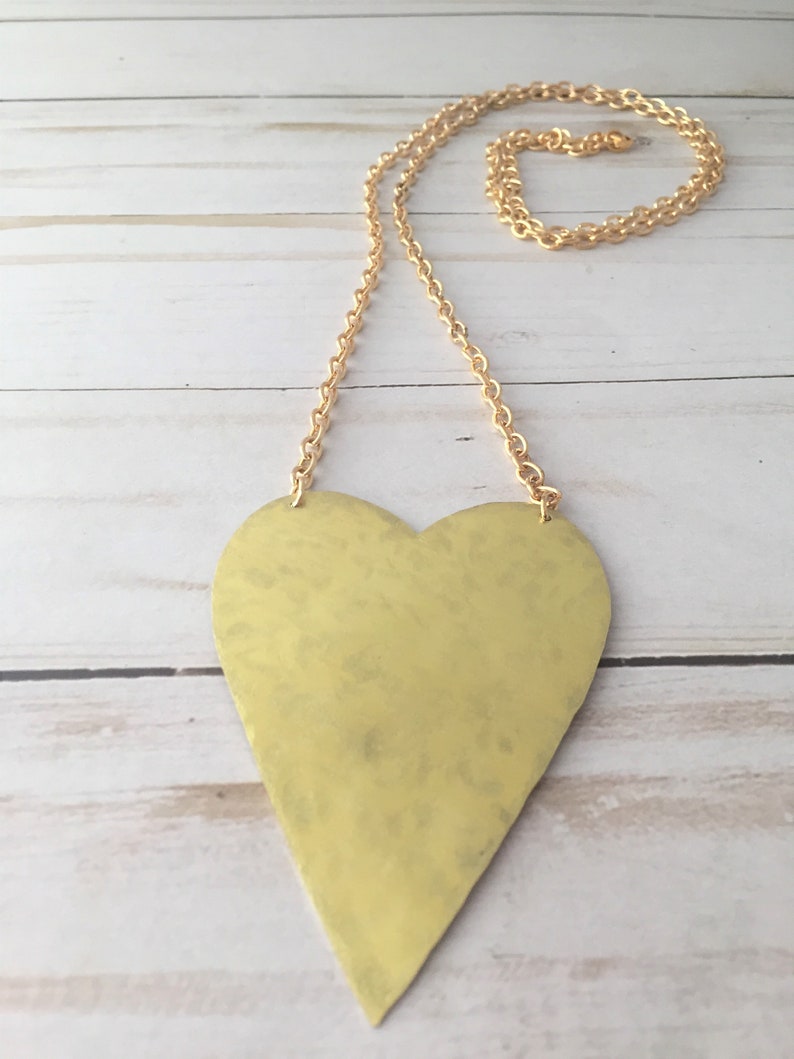 Op de afbeelding: Een gouden ketting met een hartvormige hanger met een gehammerde textuur. De ketting is ook goud.