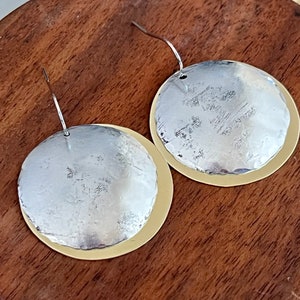 Puede incluir: Un par de pendientes redondos de plata y oro con textura martillada. Los pendientes tienen un diseño sencillo.