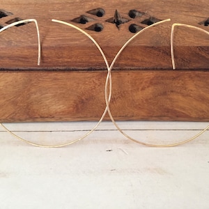 Puede incluir: Un par de pendientes de aro de oro con un diseño simple y minimalista. Los pendientes están hechos de alambre fino y tienen una forma ligeramente curvada.