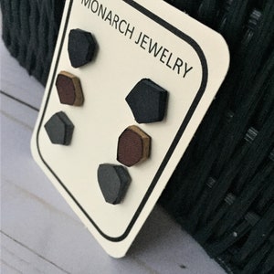 May include: A set of six geometric stud earrings on a white card with black trim. The earrings are in three colors: black, brown, and gold. The card has the text "MONARCH JEWELRY" printed on it.