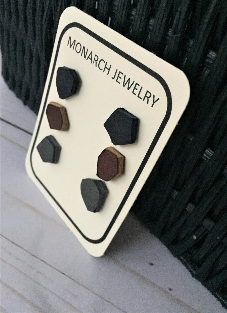 May include: A set of six geometric stud earrings on a white card with black trim. The earrings are in three colors: black, brown, and gold. The card has the text "MONARCH JEWELRY" printed on it.