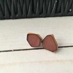 May include: A pair of small, geometric-shaped earrings made of leather. The earrings are a reddish-brown color with a gold-colored edge.