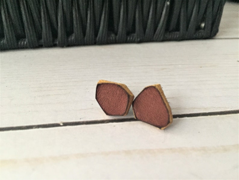 May include: A pair of small, geometric-shaped earrings made of leather. The earrings are a reddish-brown color with a gold-colored edge.