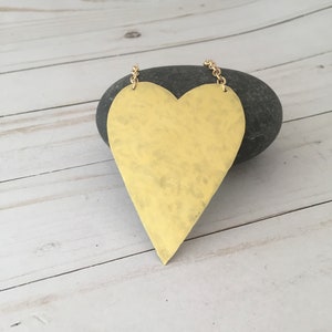 Op de afbeelding: Een grote, goudkleurige hartvormige ketting met een gehammerde textuur. De hanger hangt aan een gouden ketting.