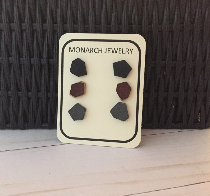 May include: A card with the text "MONARCH JEWELRY" on it. There are six small geometric shapes on the card, three on each side. The shapes are black, gray, and maroon.