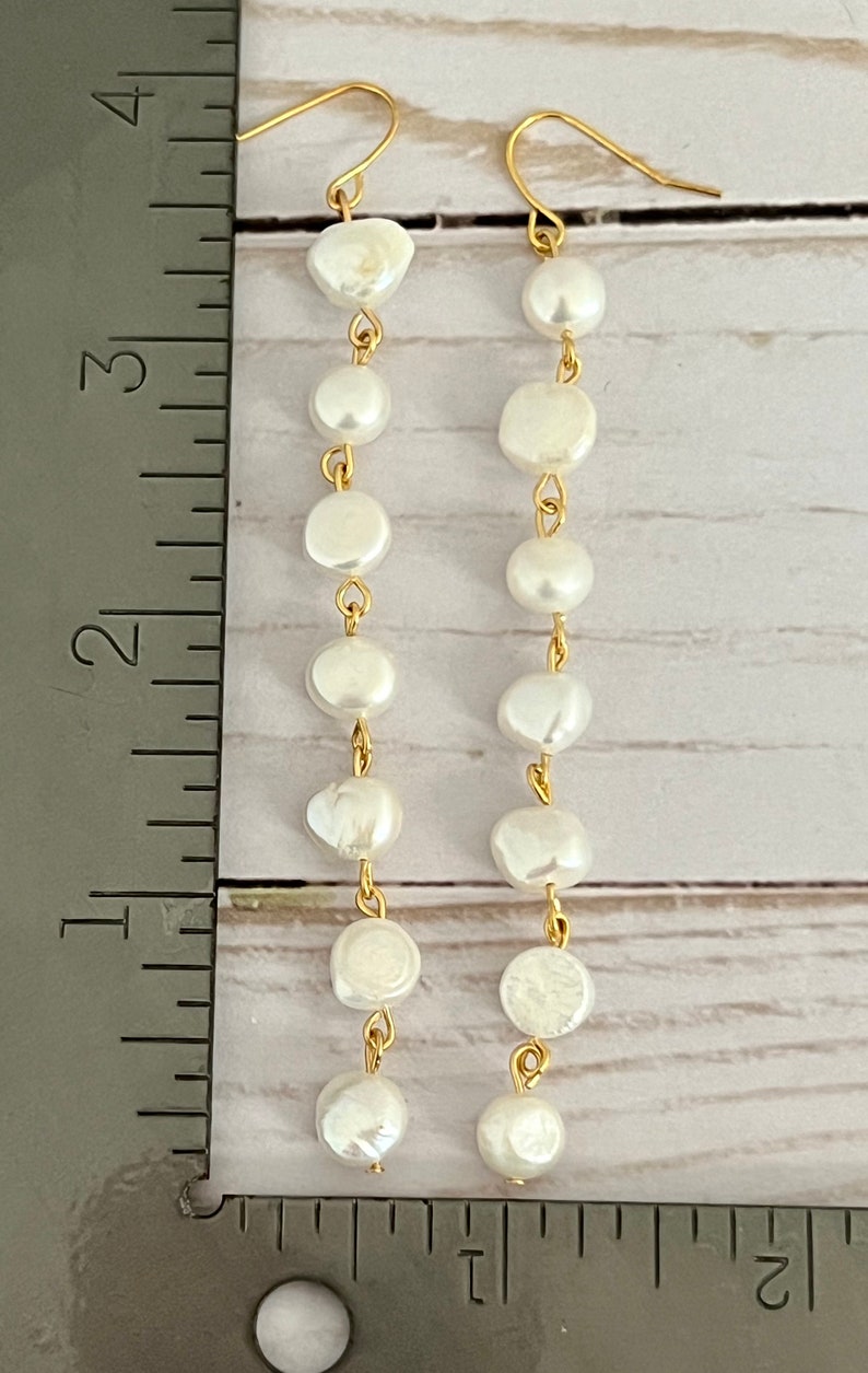 Pu&ograve; includere: Un paio di orecchini d'oro con gocce di perle bianche. Gli orecchini sono lunghi circa 7,6 cm.