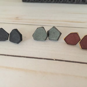 May include: Three pairs of leather earrings in black, gray, and burgundy. Each pair is shaped like a pentagon.