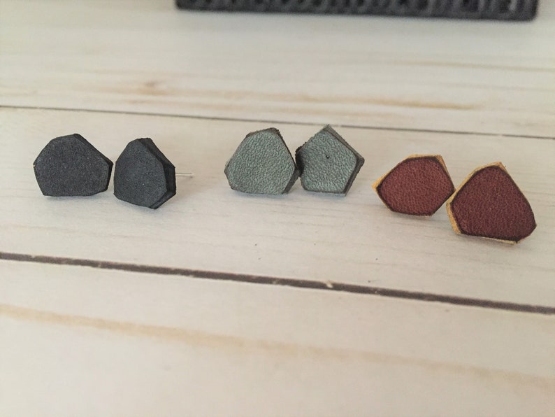 May include: Three pairs of leather earrings in black, gray, and burgundy. Each pair is shaped like a pentagon.