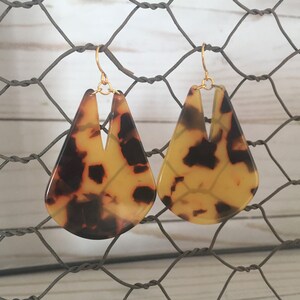 May include: A pair of gold tone earrings with a teardrop shaped tortoiseshell design.