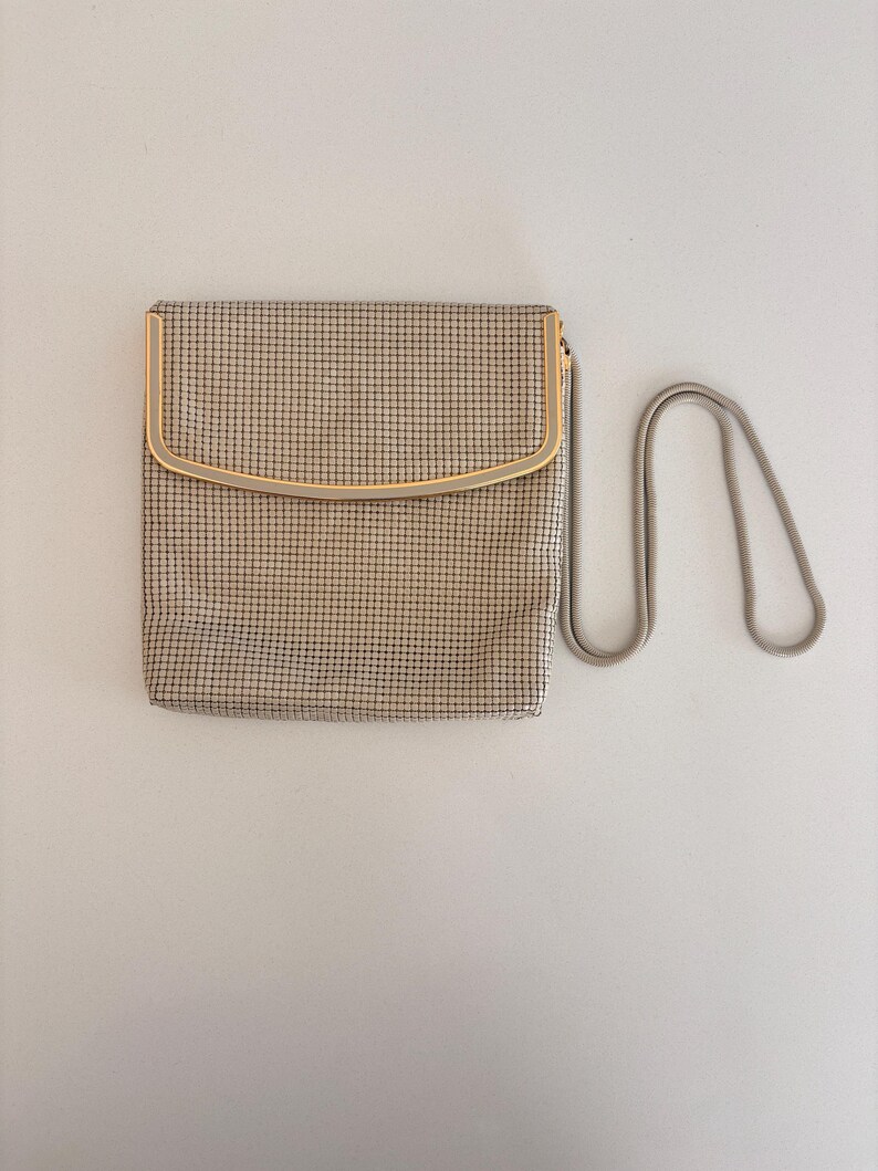Puede incluir: Un bolso de mano vintage de malla beige con un marco dorado y una correa de cadena plateada. El bolso rectangular tiene una parte superior curvada y un fino patr&oacute;n de rejilla. La cadena es un dise&ntilde;o delicado y enlazado.