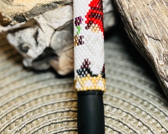 May include: A black pen with a white and red beaded design featuring a gnome with a red hat. The beads are arranged in a pattern that resembles a gnome's face and hat.