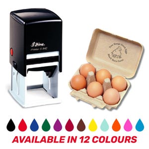 May include: A black Shiny Printer S-542 stamp beside a carton of six brown eggs. The egg carton is labelled "Free Range Fresh Eggs Black Barn Farm." Below are 12 colour options with the text "AVAILABLE IN 12 COLOURS."