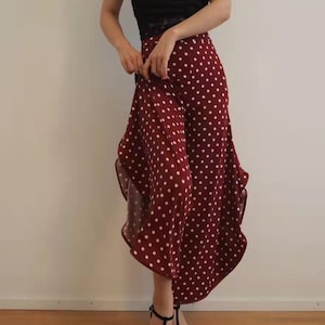 Puede incluir: Un top negro sin mangas combinado con pantalones de cintura alta y pernera ancha en color burdeos con lunares blancos. Sandalias negras de tacón completan el conjunto. El conjunto es adecuado para diversas ocasiones. El pantalón mide unos 100 cm de largo.