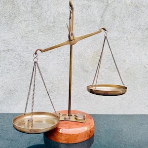 May include: A vintage brass balance scale with two circular pans suspended by chains. The scale is mounted on a wooden base with a brass support. The scale is a decorative item.
