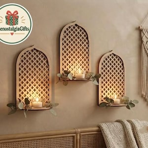 Peut inclure: Trois appliques murales en bois en forme d'arche avec des découpes en treillis complexes, chacune dotée d'une petite étagère supportant une bougie chauffe-plat blanche allumée et un feuillage vert décoratif sur un mur uni.