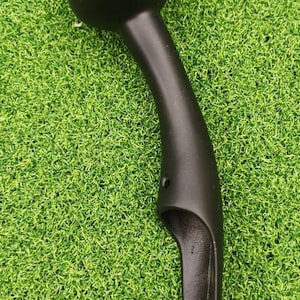 May include: A black, curved handle with a rounded top and a flared base. The handle has a smooth, matte finish and appears to be made of a solid material. The object is set against a backdrop of artificial green grass.