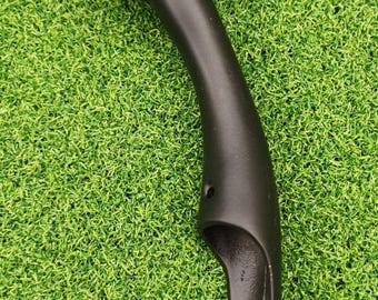 May include: A black, curved handle with a rounded top and a flared base. The handle has a smooth, matte finish and appears to be made of a solid material. The object is set against a backdrop of artificial green grass.