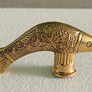 Puede incluir: Un tirador decorativo dorado con forma de pez. El tirador presenta intrincados diseños florales y de hojas en el cuerpo del pez. El tirador está diseñado con una base cilíndrica.